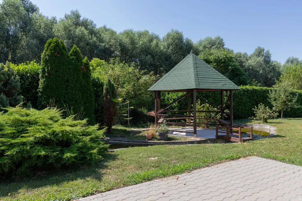 Drvena vrtna sjenica s mostićem preko jezerca, iza nje šuma
